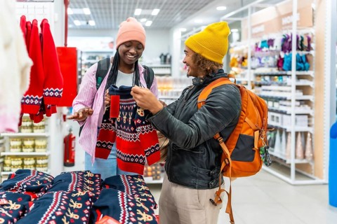 Happy young multiracial couple smiling as they browse and select red holiday sweaters in a busy