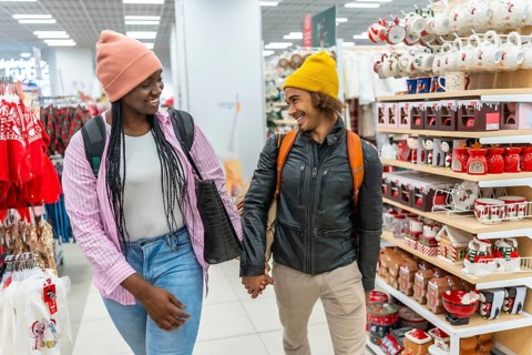 Diverse young couple smiling while holding hands, shopping together in a store, browsing shelves