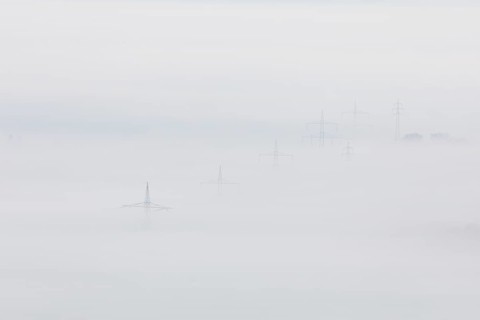High-voltage pylons rise up from the thick sea of fog, silence and technology the silhouette of
