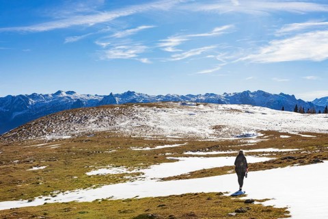 Female hiker walks across a snowfield on the Trattberg Alm with a view of the Tennengebirge,
