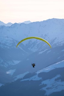 Paragliders flying over snowy mountain peaks in winter in evening light, KitzbÃ¼hel Alps, Tyrol,