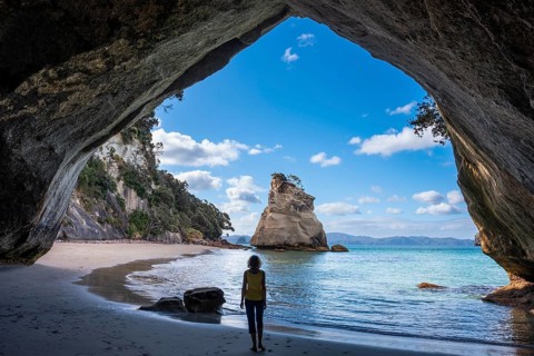 A woman in Cathedral Cove in New Zealand. Sea, sandy beach and limestone cliffs. The cave itself