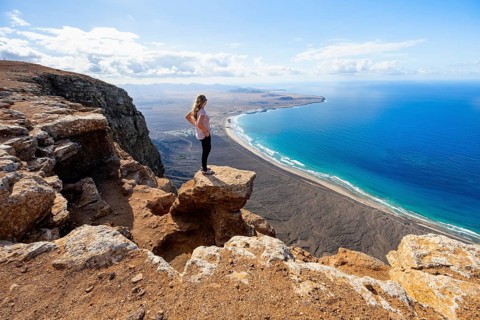 Young woman enjoying the view from the Risco de Famara cliffs to Famara beach, Playa de Famara with