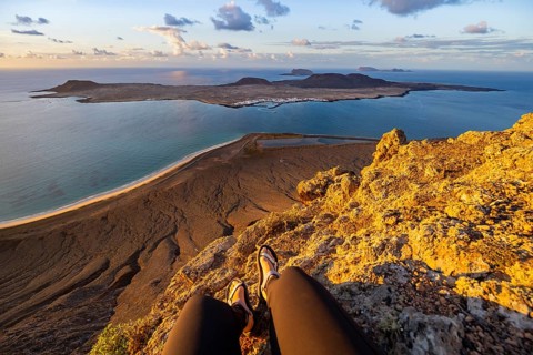 First person view, legs of a woman sitting on a steep cliff, view of the sea and the island of La