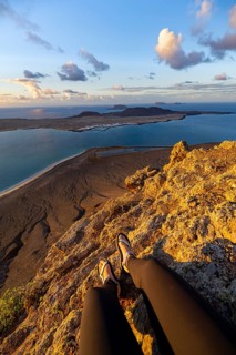 First person view, legs of a woman sitting on a steep cliff, view of the sea and the island of La