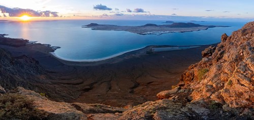 View of steep cliffs to sea and the island of La Graciosa with sun stars, Mirador del Porrito