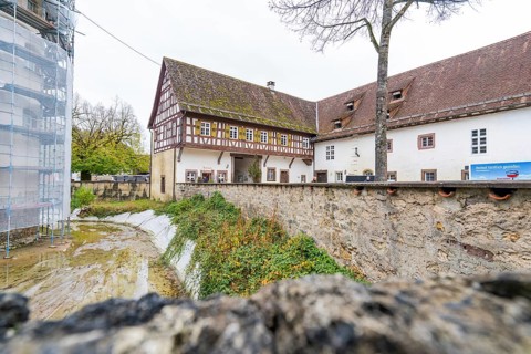 Traditional half-timbered house with moss-covered roof next to an old stone wall, Wasserschloss