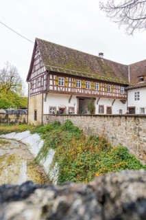 Well-preserved traditional half-timbered house next to a stone wall in a rural area, Wasserschloss