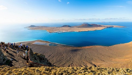 View of La Graciosa island with volcanic craters in the evening light, tourists on an observation