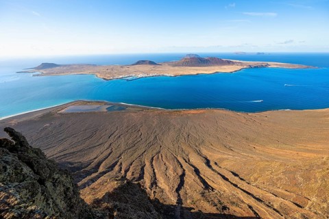 View of steep cliffs by the sea and island of La Graciosa with volcanic craters in the evening
