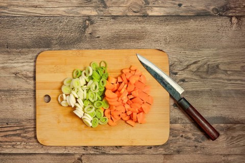 Fresh leek onion and carrots are chopped and neatly arranged on a wooden cutting board. A sharp
