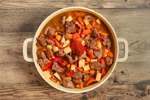 Tender beef chunks are mixed with vegetables like carrots, bell peppers and celery root in a pot.
