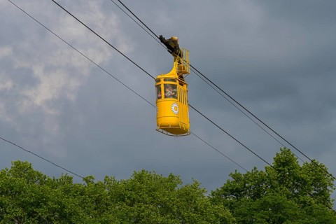 Yellow cable car floating over green trees under cloudy sky, cable car cabin, Kutaisi, Imereti