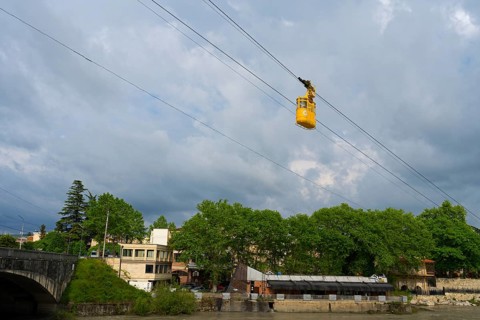 Yellow cable car crosses river, in the background a cloudy city, cable car cabin above the Rioni