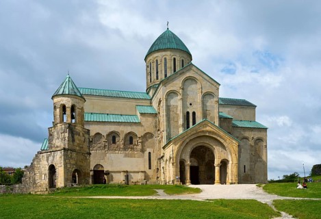 An impressive cathedral with green domes under a cloudy sky in a meadow, Bagrati Cathedral, Church