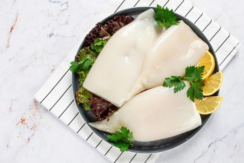 Fresh squid on a black plate with greens and lemon slices prepared for cooking in a kitchen setting