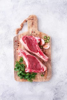 Fresh pieces of beef on the bone, on a wooden cutting board, with herbs and spices, ready for