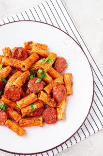 Rigatoni pasta with spicy sausage, and rich tomato sauce served, on a white plate, homemade