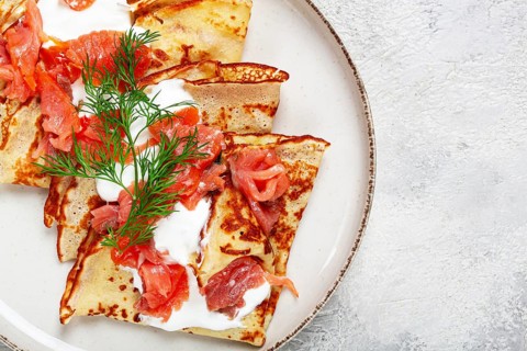Delicious pancakes with salmon and sour cream, breakfast, on a plate, rustic style, with cutlery