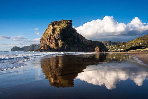 Landscape in New Zealand with sea and sandy beach. Piha Beach and Lion Rock. People on the beach,