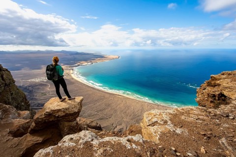 Young woman enjoying the view from the Risco de Famara cliffs to Famara beach, Playa de Famara with