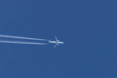 Jet passenger aircraft flying in a blue sky with contrails or vapour trails behind, England, United