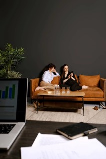 Two individuals are seated comfortably on a stylish couch, one looking at a phone while the other