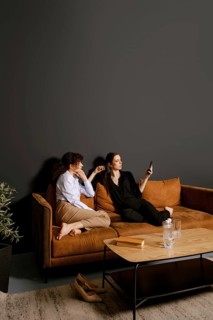 Two friends sit on a comfortable couch in a stylish living room. One is scrolling on a smartphone