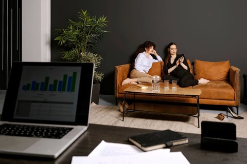 Two friends sit comfortably on a brown couch in a stylish living room, engaging with a smartphone.