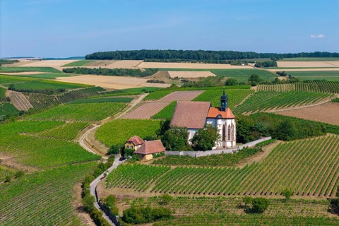 Pilgrimage church Maria im Weingarten, surrounded by green hills and fields under a sunny sky,