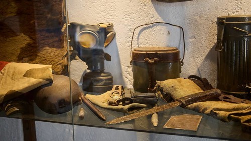 Display case with gas mask, helmet and other military collectibles, cookware, knife, pistol, war
