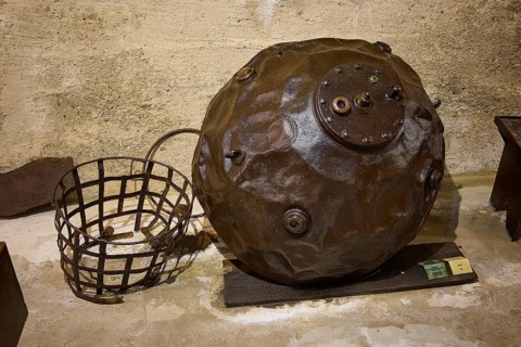 An ancient sea mine next to a metal basket on a concrete floor, War Museum, Military Museum, Tunnel