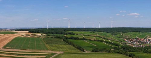 Panoramic view of fields with a wind farm in the background under a blue sky, aerial view,