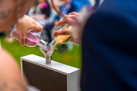 Bride and groom performing the sand ceremony ritual, pouring colorful sand into a glass container