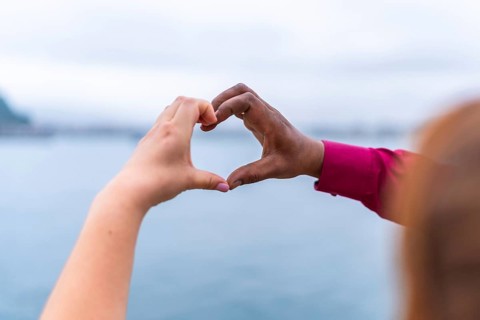 Bride and groom forming a heart shape with their hands against a stunning seascape, celebrating