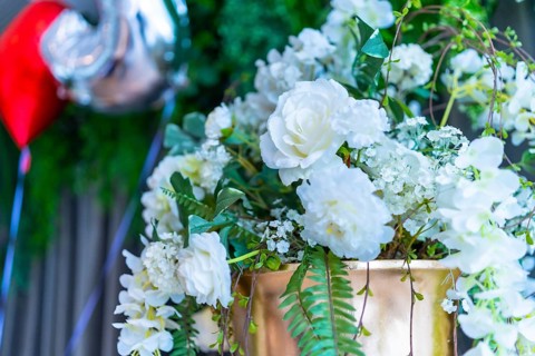 Elegant white roses and greenery adorn a golden vase, adding a touch of romance to a wedding