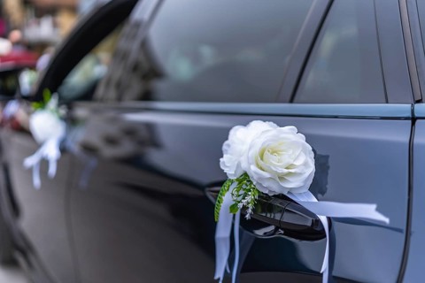 White roses and ribbons elegantly adorn a wedding car door handle, adding a touch of romance and