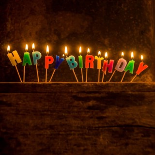 Brightly lit birthday candle arrangement spelling out Happy Birthday on a rustic wooden surface for