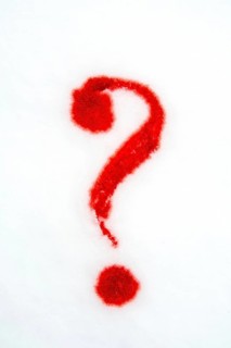 A vibrant red question mark is formed on a plain white surface using red powder, enhancing visual