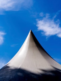 Exhibition tent under a bright blue sky adorned with fluffy clouds in a lively outdoor setting