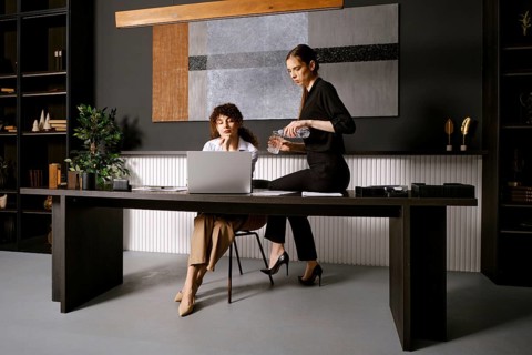 In a stylish office, two women engage in a collaborative discussion. One woman sits at a sleek