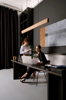 Two businesswomen are engaged in a discussion at a sleek office desk. One is seated while reviewing
