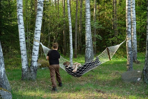 Two children enjoy their time outdoors, one relaxing in a hammock suspended between two trees while