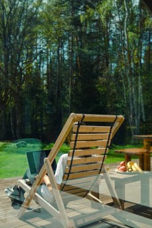 A person enjoys leisure time on a wooden lounge chair, surrounded by picturesque trees and a calm
