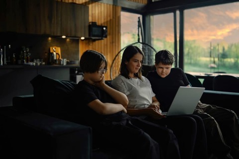 Young mother and her sons watch a series on a laptop sitting in the evening in a cozy living room