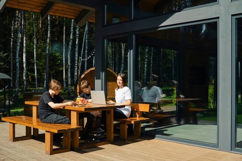 Two children and their mother are seated at a wooden table outside a modern building. They are