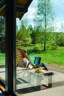 A person enjoys a peaceful moment outdoors, seated in a wooden lounge chair. Surrounded by lush