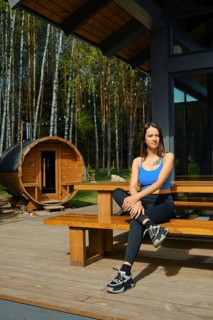 A woman dressed in casual sportswear sits comfortably on a wooden bench in front of a traditional