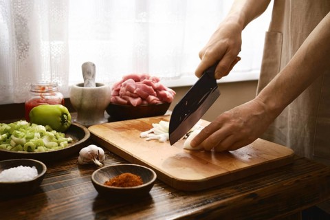 A chef finely chops onion on a wooden cutting board in a warm kitchen. Fresh ingredients like
