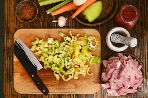 Freshly chopped green bell peppers, celery, and carrots are arranged on a wooden cutting board next